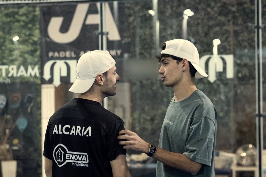A coach talks to a player up close, a hand on his shoulder, on an indoor court
