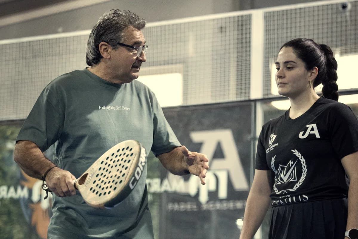 A coach corrects a player’s stroke, racket in hand