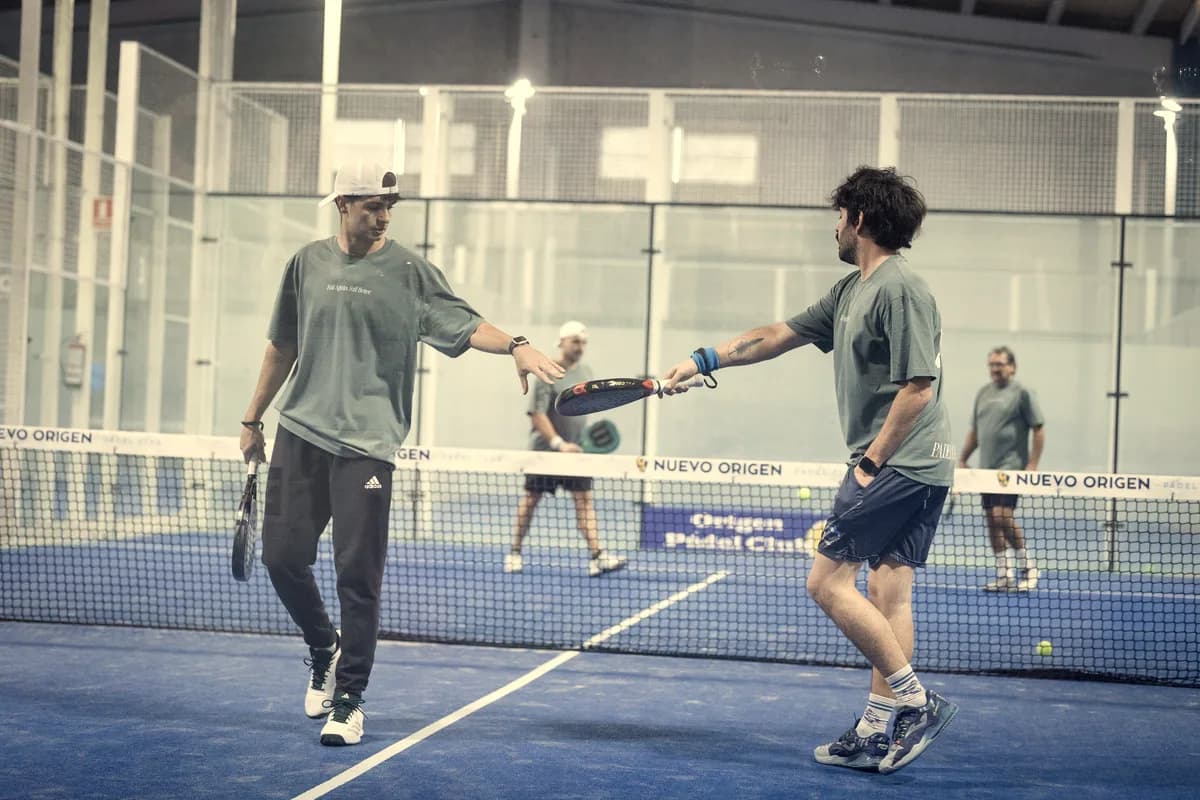 Two players tap rackets at the net on an indoor court