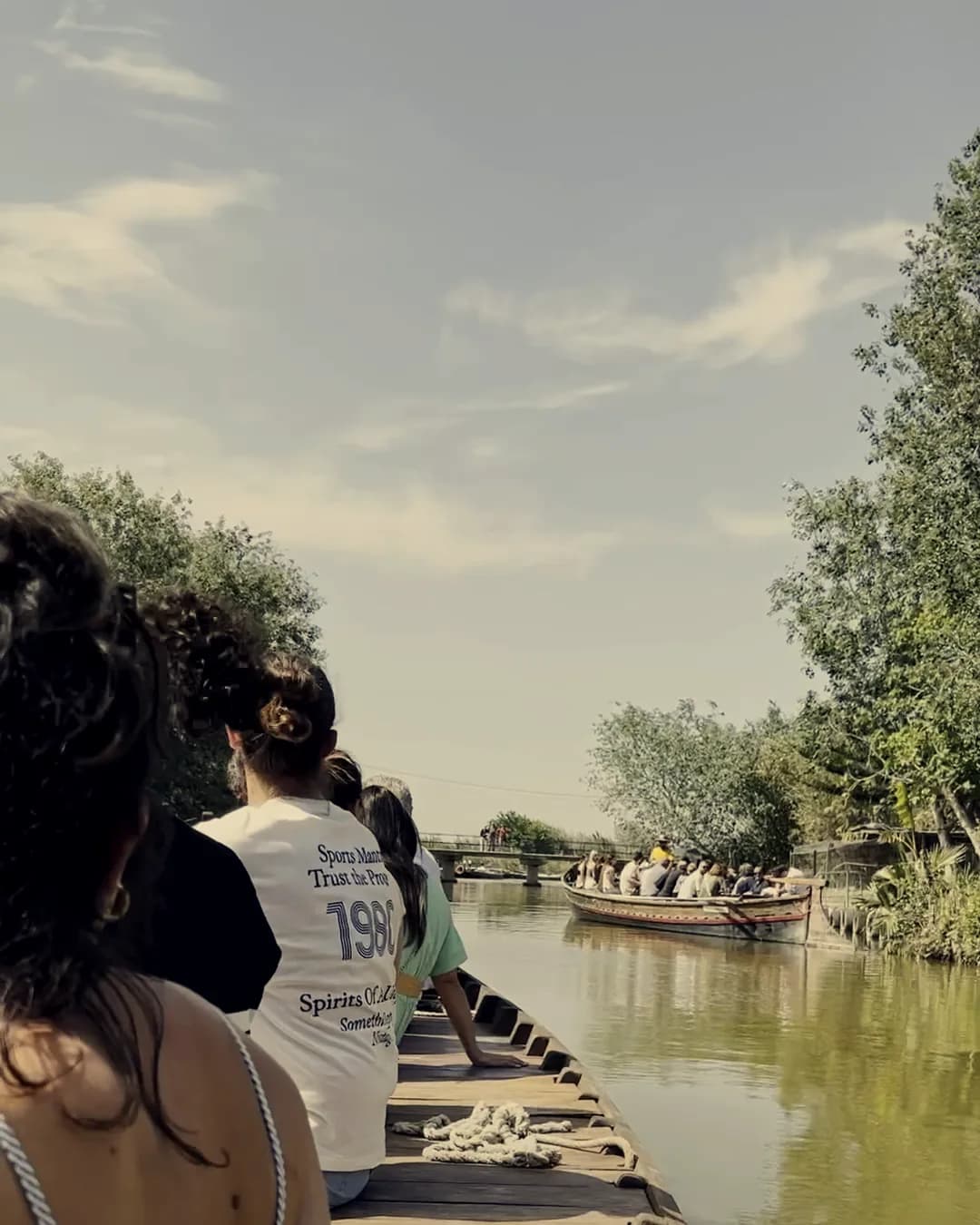 Un grupo, de espaldas, en una barca por un canal de la Albufera, con otra barca delante