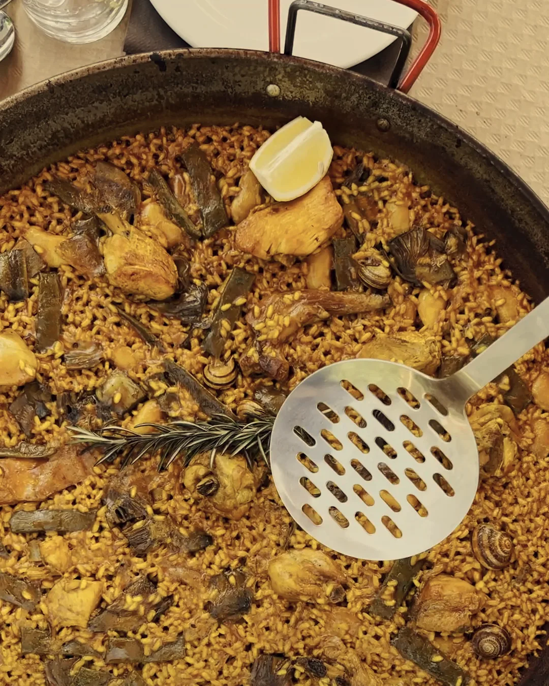 Una paella valenciana vista desde arriba, con la paleta y un trozo de limón