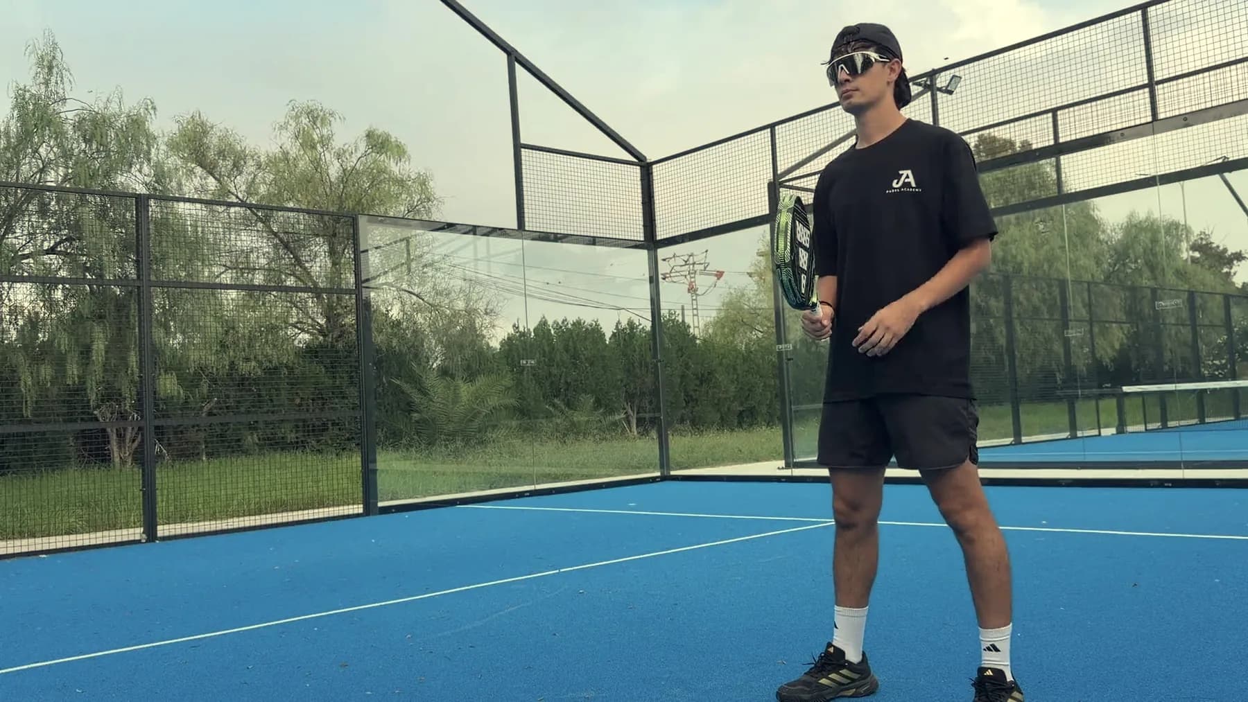 A player holding a racket on a blue outdoor court at Saladar, with trees behind