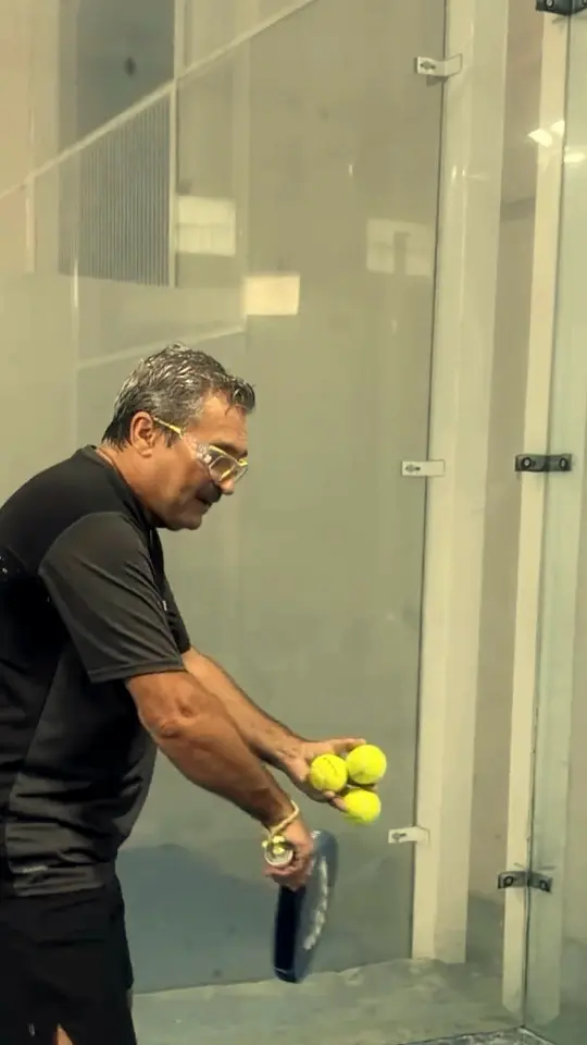 Un entrenador de JA, con la pala y la bola en la mano, en una pista azul cubierta.