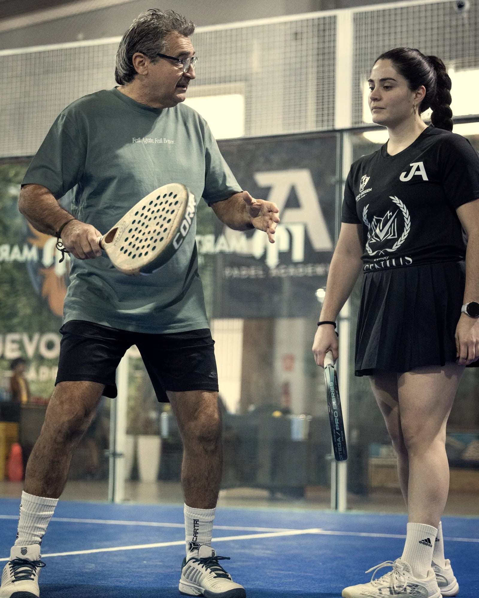 A coach corrects a player’s stroke, racket in hand
