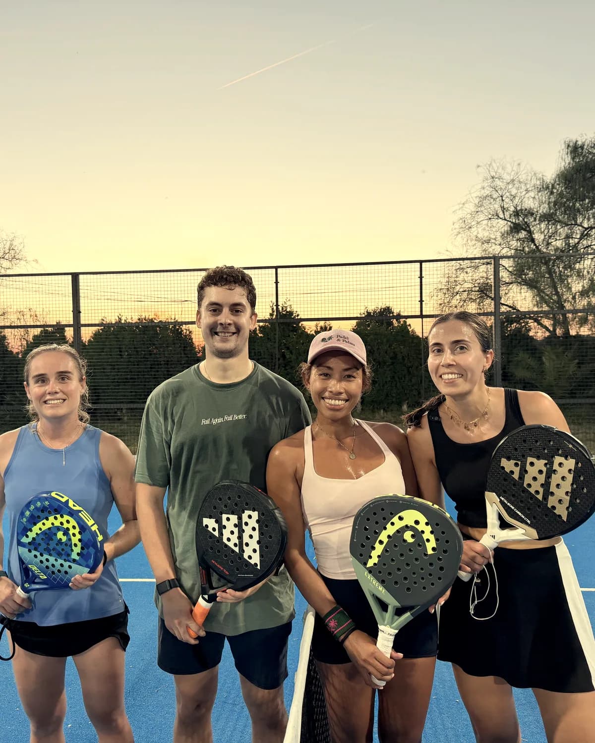 Cuatro jugadores sonríen con sus palas junto a la red al atardecer